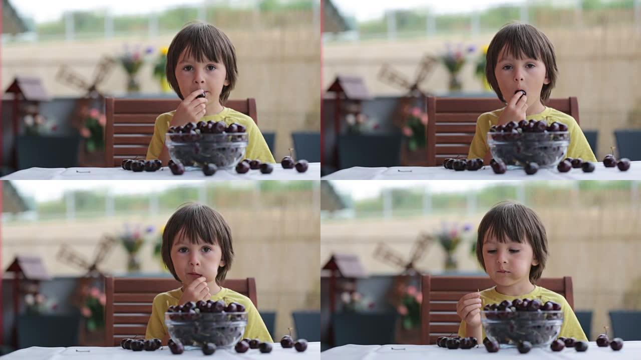 可爱的小男孩，在户外吃甜樱桃，坐在桌子上