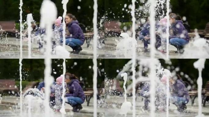 幸福的家庭-城市公园喷泉附近的母亲，父亲和宝贝女儿-女孩碰水