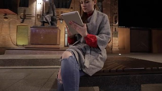 年轻女子触摸平板电脑，坐在秋天的街道长椅上。