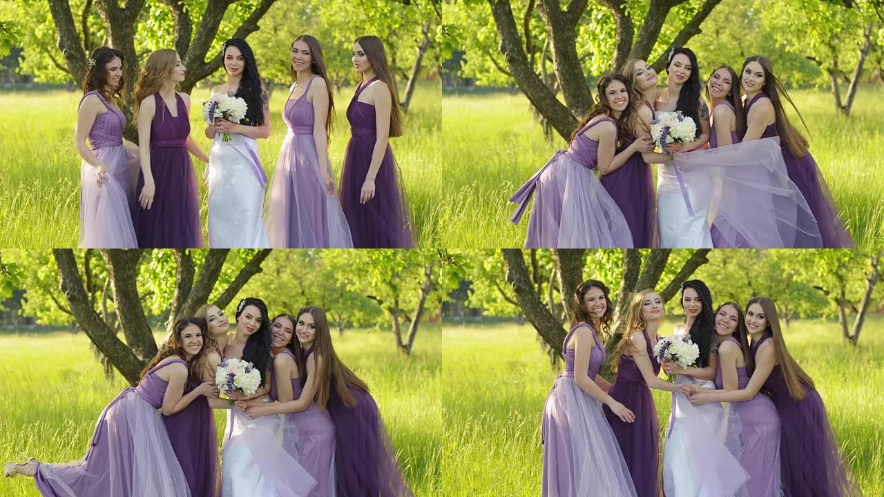 情感伴娘拥抱新娘。穿着紫色婚纱的高加索女孩微笑着在户外摆姿势。