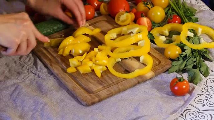 女人在厨房做饭。将黄胡椒倒入小方块中。桌子上有很多不同的蔬菜。多汁成熟的西红柿和黄瓜