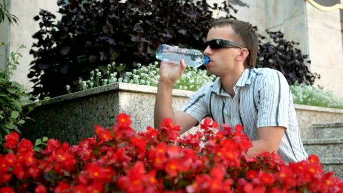 口渴的人休息一下，喝一瓶水。戴着墨镜和夹克的男人。靠近很多红花
