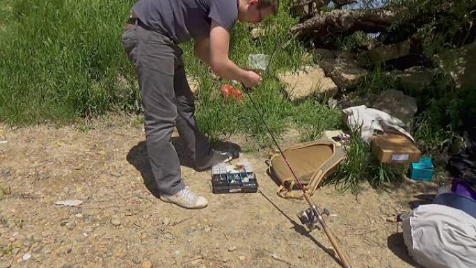 一个戴眼镜的人将钓鱼设备固定在钓鱼竿上。渔具。带钓鱼设备的塑料盒。库班河