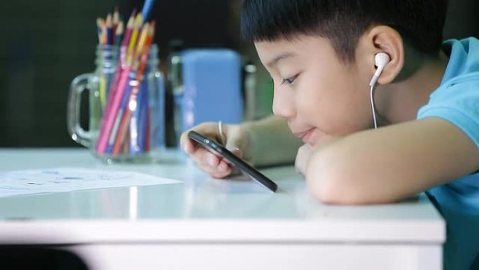 亚洲儿童在智能手机上使用带耳塞的数字平板电脑。