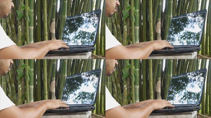 男子在竹树下使用笔记本电脑