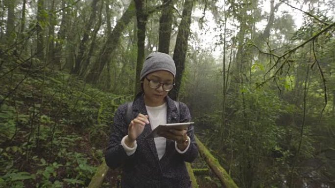 亚洲妇女在雨林中旅行使用数字平板电脑拍照