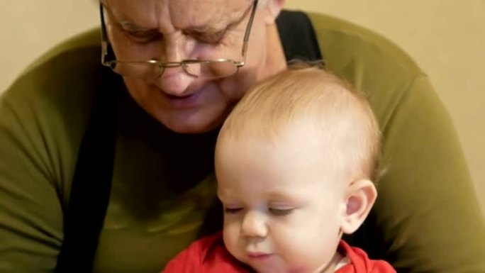 有吸引力的婴儿画与他的祖父在纸上的标记。一个男孩坐在他爷爷家里的腿上。孩子1年