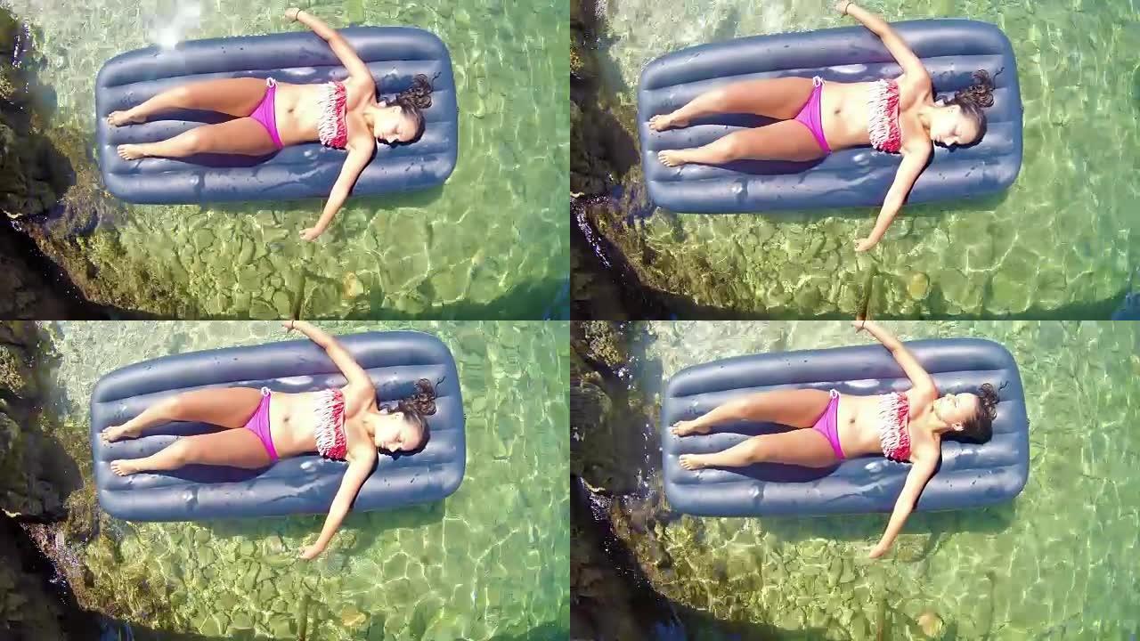 夏天的概念，美丽的女人躺在lilo在她的假期在干净的海水。UHD俯视图