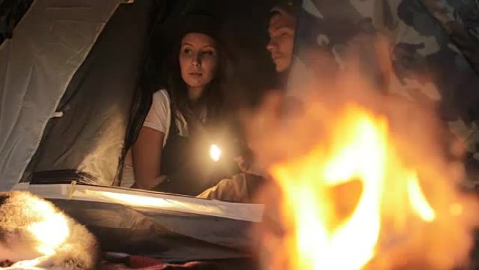 夫妇在帐篷里，手电筒靠近火