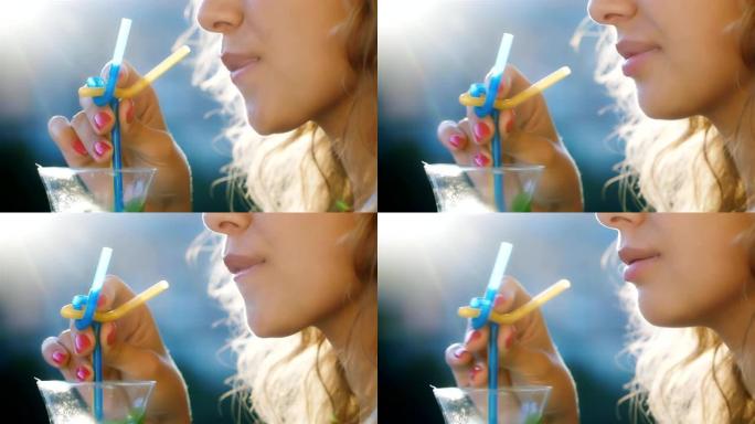 年轻的女人在杯子里搅拌饮料。在图片中，可见阳光照耀的嘴唇和头发。概念-天堂般的假期