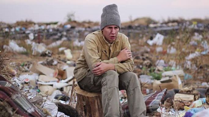 肮脏的无家可归者坐在垃圾桶的树桩上，想着生活