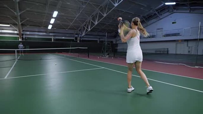 白色的运动员在室内球场进行网球比赛时将球扔过网，女子正在用球拍积极移动