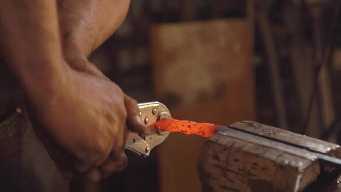 处理熔融金属特写。手工铁匠。人在夹在虎钳中的铁上形成图案。慢动作