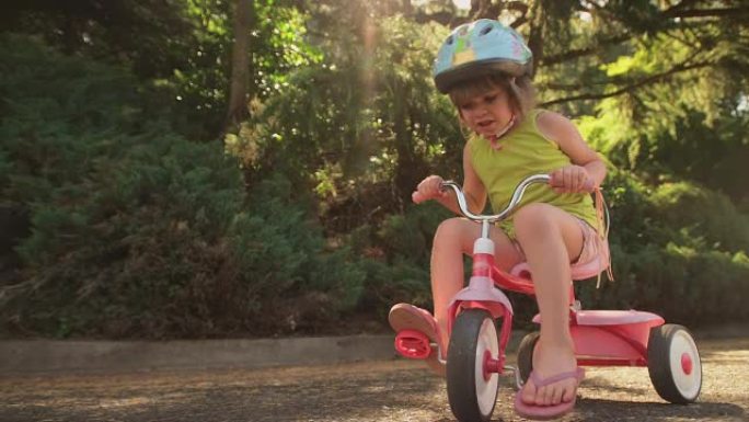 一个可爱的小女孩坐在她的三轮车上，微笑着，然后骑车离开