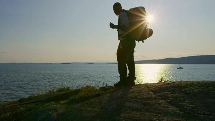 日落时，背包在海边的山上露营的活跃男子