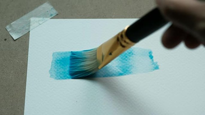 艺术家的特写镜头用画笔在水彩纸上200 GSM的水彩画蓝色矩形。