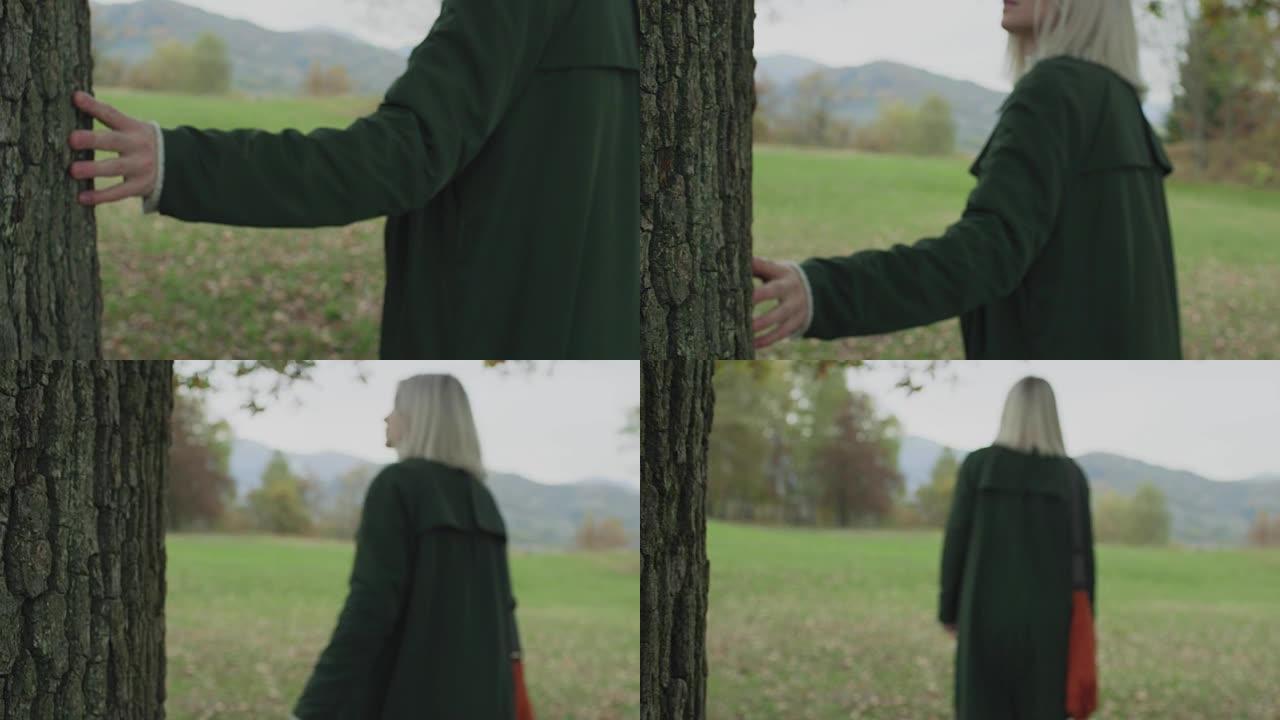 躯干和手上的细节。高加索金发女子斯洛莫走向秋天的树林，触摸树。在万向节后面。讲故事真正的年轻成年人独