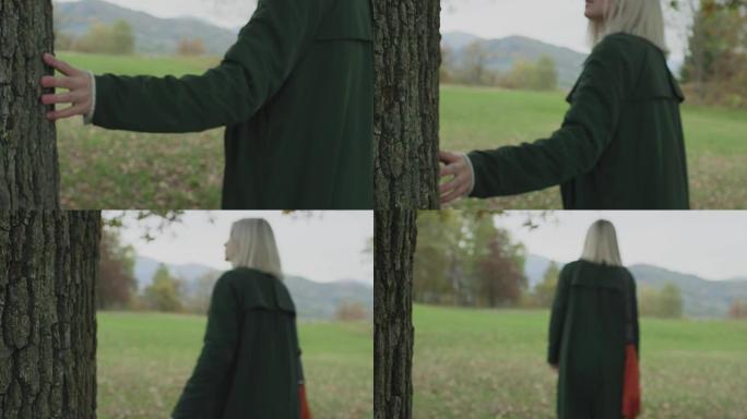 躯干和手上的细节。高加索金发女子斯洛莫走向秋天的树林，触摸树。在万向节后面。讲故事真正的年轻成年人独