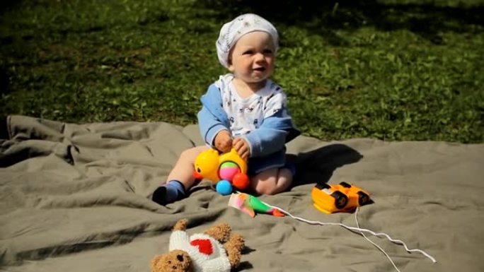 可爱的俏皮微笑金发1岁男孩坐在绿草地上户外玩玩具