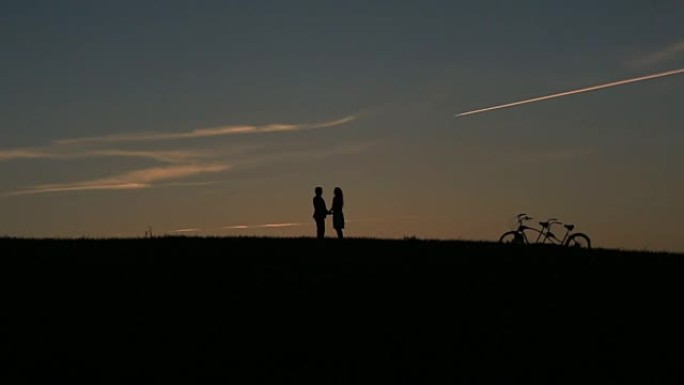 神话般的情侣与双人自行车的剪影在日落时手牵着手跳跃