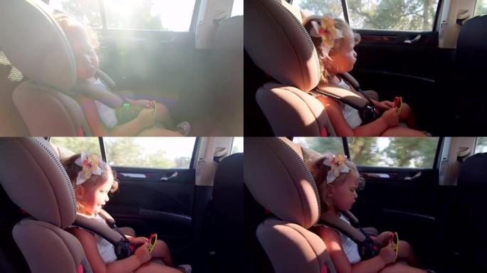 漂亮的小女孩在旅途中坐在汽车的儿童后座上唱歌