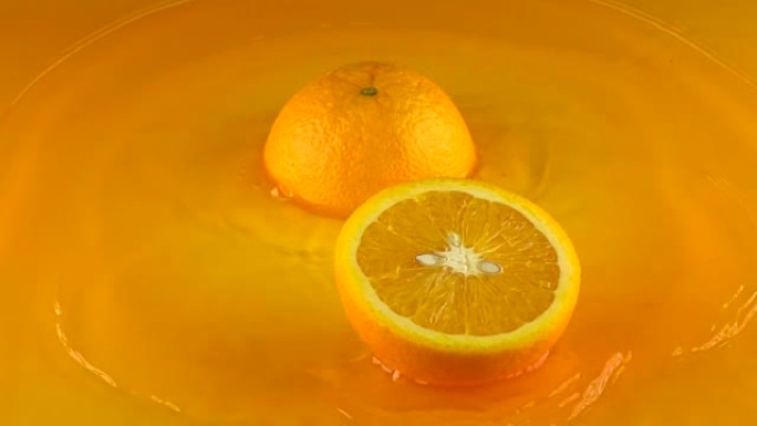 橙子击中橙汁表面并分成两半。慢动作视频