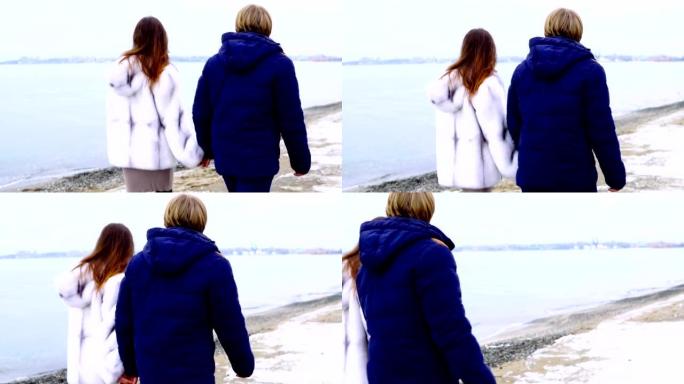 情侣手牵着手在沙滩上散步。浪漫的情侣穿着外套在沙滩上散步。慢动作