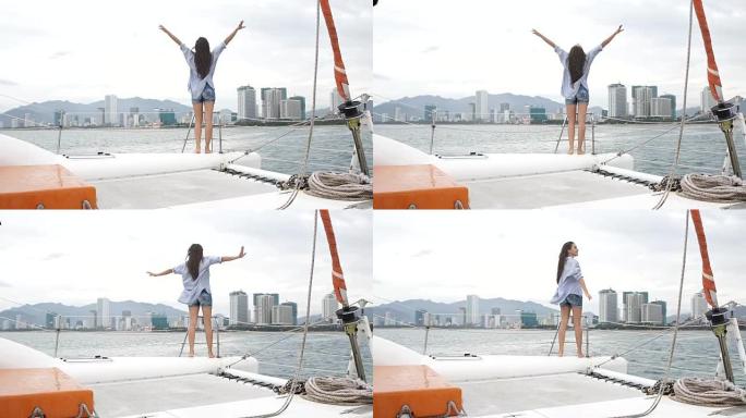 年轻女子在享受双体船巡游时看着大海，举起双手
