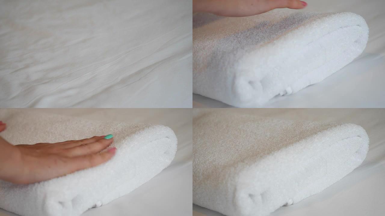 女性双手的特写镜头，用白色床单把新鲜干净的毛巾放在床上