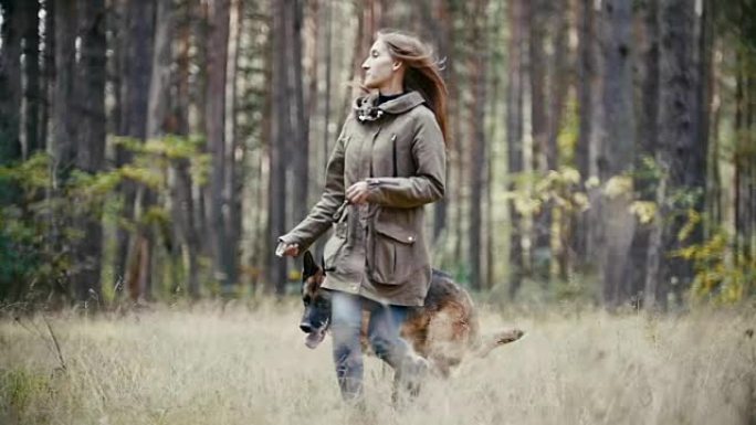 年轻女子与牧羊犬在秋天的森林中奔跑，慢动作