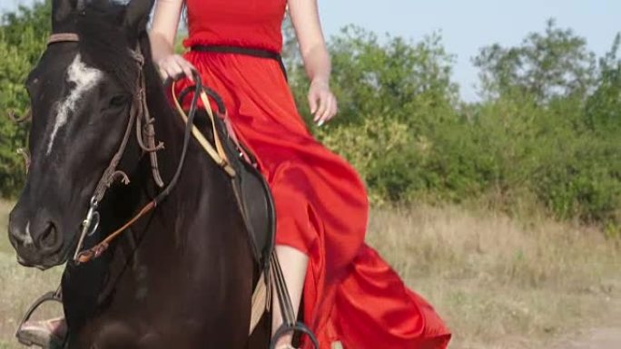 年轻的金发女孩穿着鲜艳的红色长裙骑着黑马