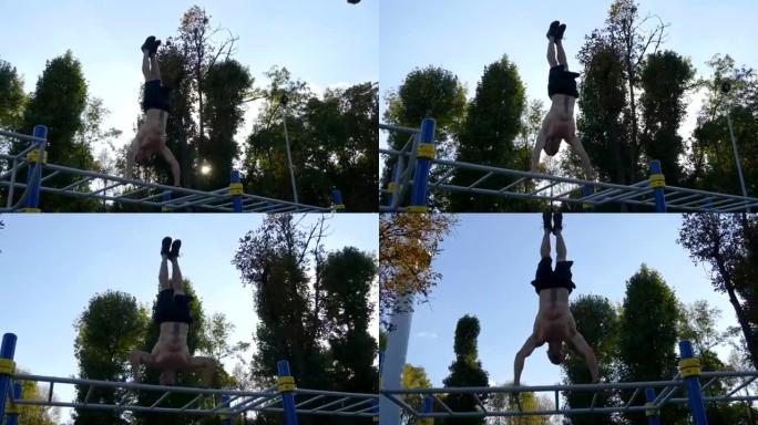 强壮的肌肉男人在公园倒立。适合肌肉发达的男性健身男子在室外单杠上做特技。运动员训练在室外肌肉处进行倒