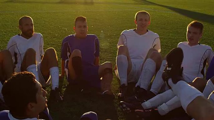 日落时坐在一个圆圈里玩有趣游戏的足球队