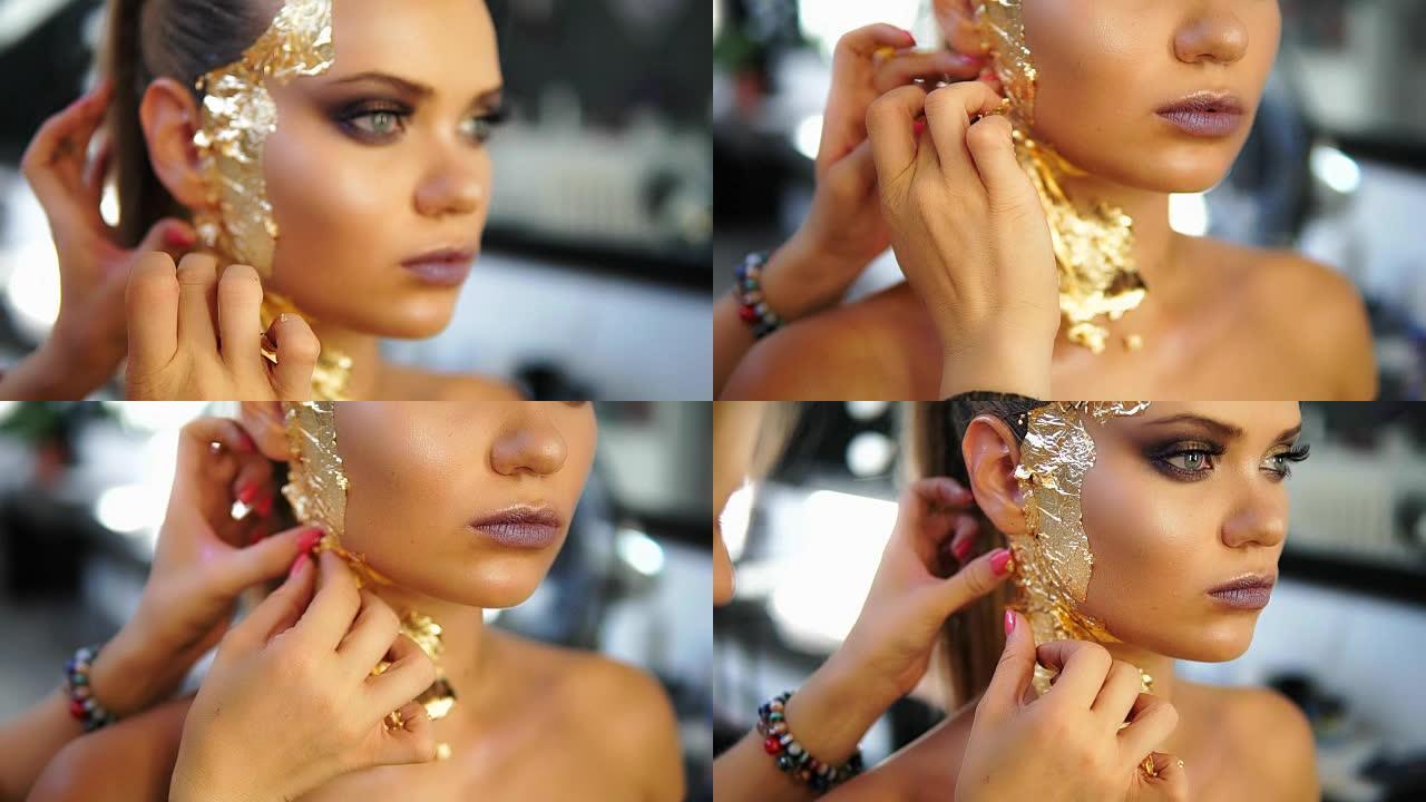 一名化妆师在模特脸上涂抹金色闪亮的金属纸的特写镜头。为时装秀做准备。模特试衣间