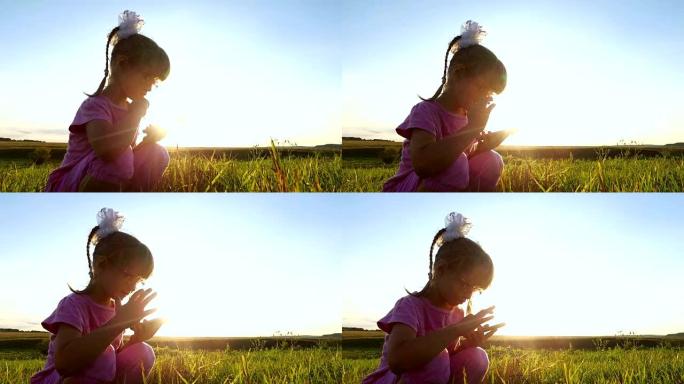 热情的小女孩在智能手机上玩。戴眼镜的女童坐在绿色的草地上。