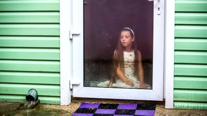 悲伤的女孩坐在玻璃门前看着雨