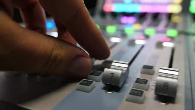 录音棚里的一个人在调音台上工作，他正在拉起旋钮，镜头从左向右移动