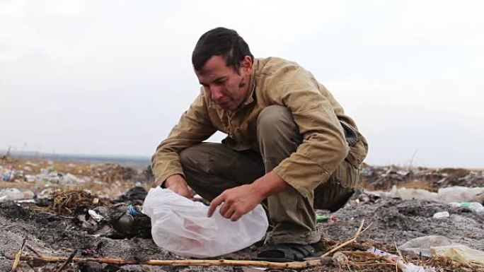 肮脏的无家可归者坐在垃圾的特写镜头上，从袋子里吃面包