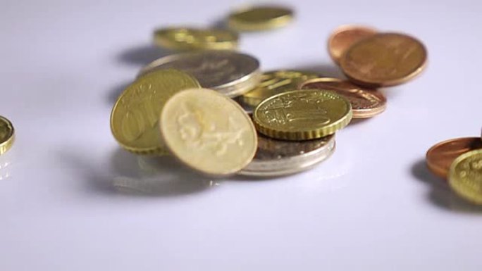各国硬币的货币和价值落在白色的反光表面上，慢动作。金钱、商业、收入概念。