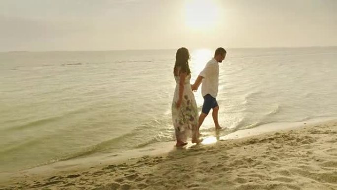 一起快乐。一对年轻夫妇在日落时的夏雨下在海边散步
