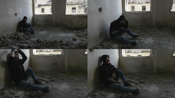 蒙面沮丧的年轻人坐在一栋废弃的建筑物中