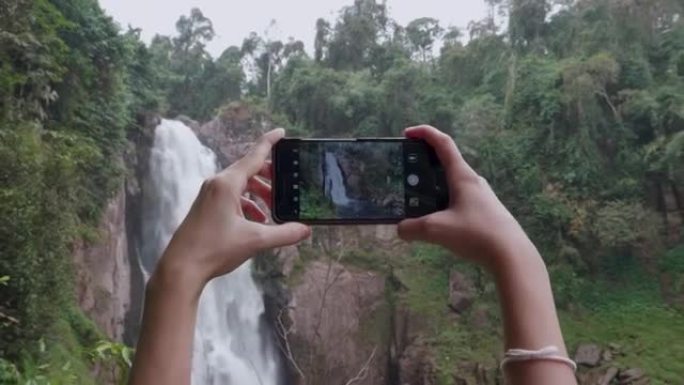 妇女在考艾国家公园瀑布用智能手机拍照
