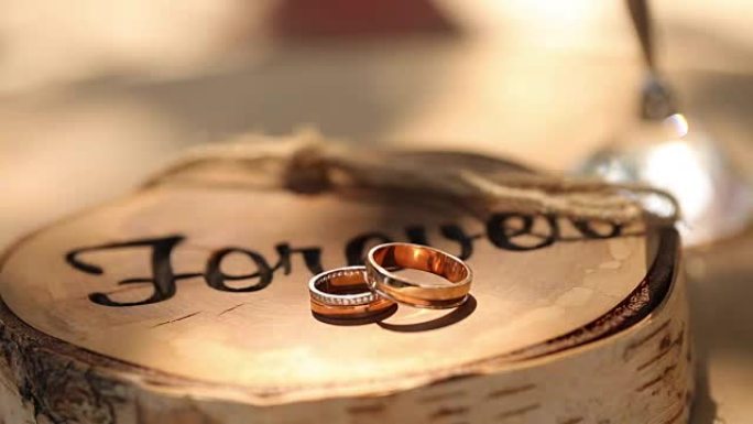 结婚戒指躺在树桩上的木制乡村风格的架子上，在新郎和新娘的仪式上刻有 “永远” 字样