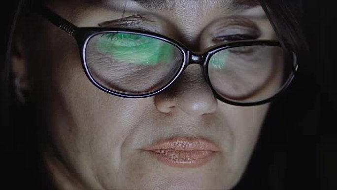 一个戴眼镜的女人看着平板电脑的屏幕。周围很暗。