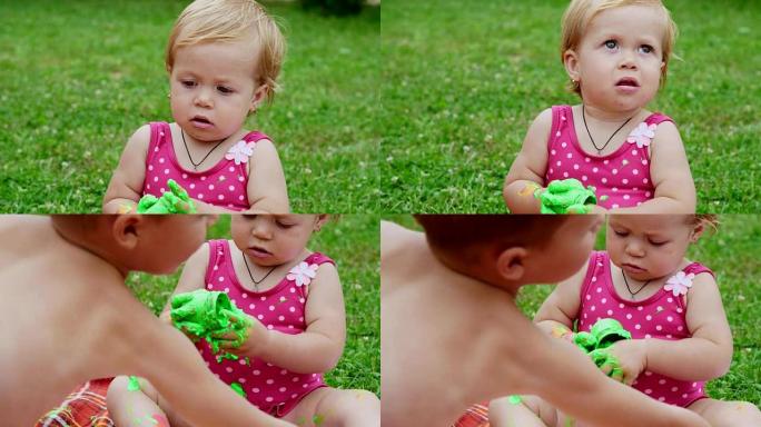 一个小孩，一个一岁大的女孩在玩耍，用手指画绘画，装饰自己，在花园里，坐在毯子，床罩上，在草地上，在草