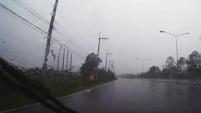 通过带有雨滴的汽车挡风玻璃的道路视图，在雨中行驶。