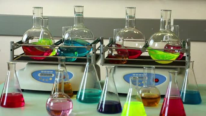 带有彩色溶液的实验室玻璃器皿在两个振动器上旋转，一些烧瓶站在前面