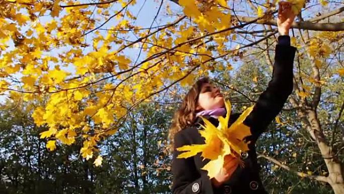 在秋天的公园里，一个女孩从树枝上扔下黄叶