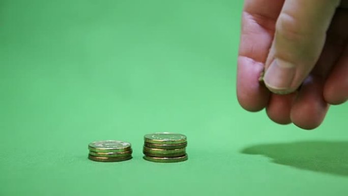手将一叠硬币放在绿色背景上