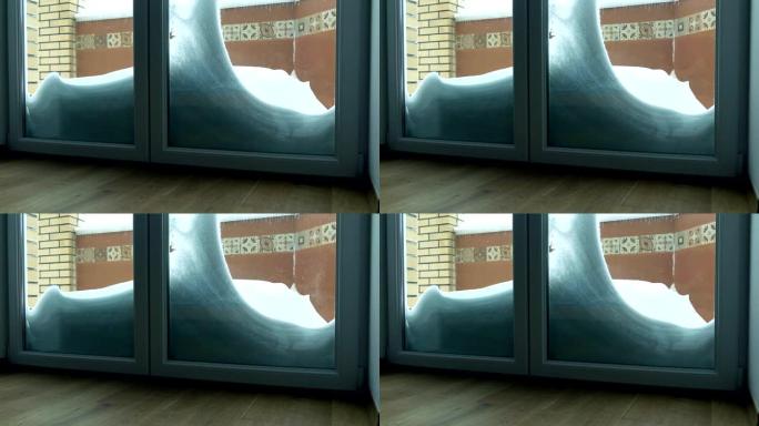 玻璃门后面的雪堆和冰柱。温暖、寒冷和绝缘概念。全高清镜头